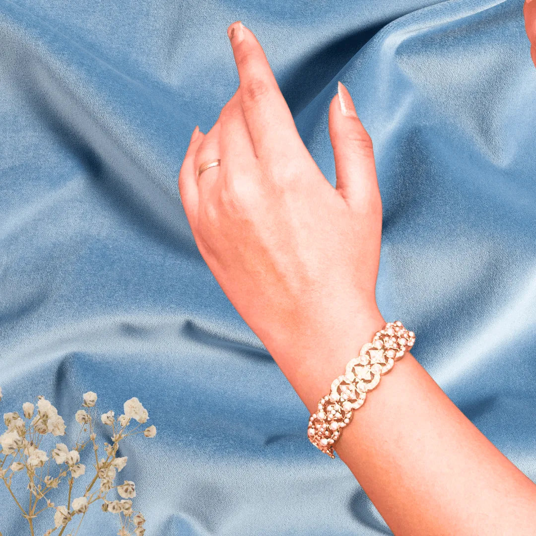 gold plated jadau bracelet wearing hand on a blue fabric background with small white flowers.