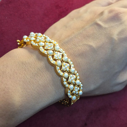 jadau bracelet with pearls on a wrist against a maroon background