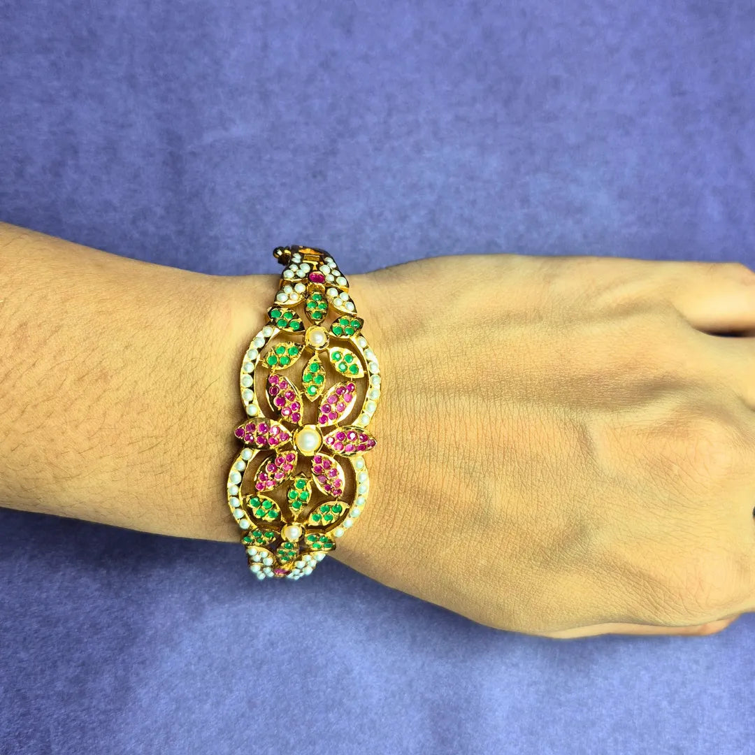 floral jadau bracelet with green and pink stones on a wrist against a blue background