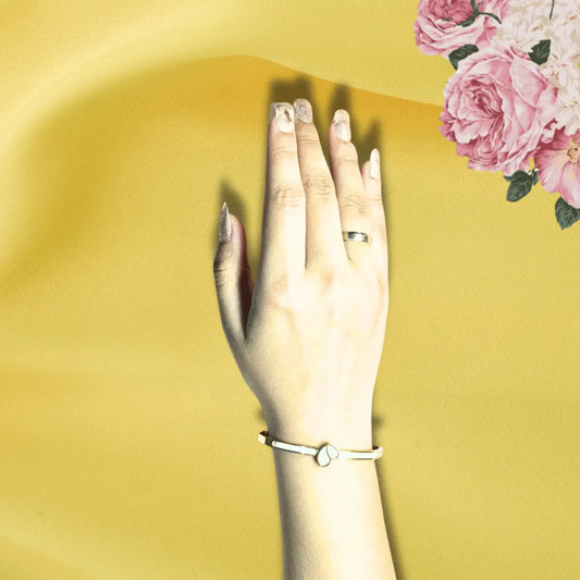 Gold plated bracelet for women with heart detail worn on wrist against yellow background with pink flowers