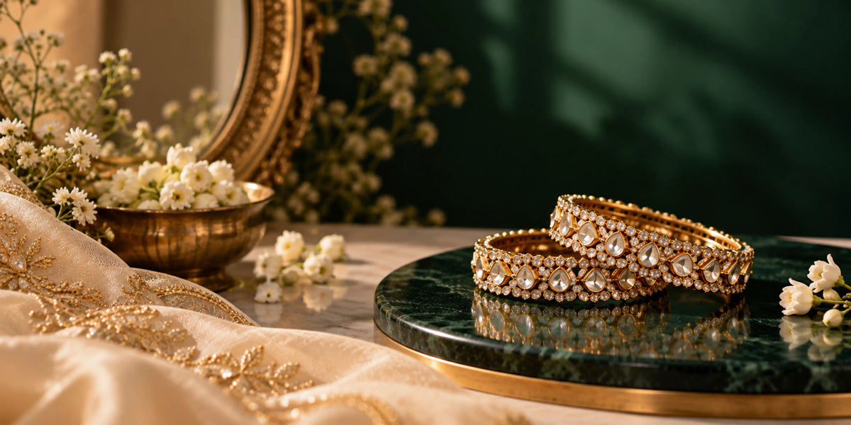 Gold stone-studded bangles displayed on a dark green marble stand with cream fabric and white flowers