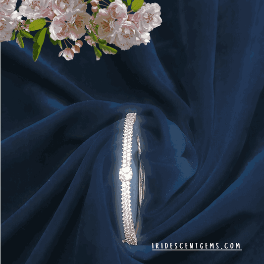 Graceful jewelry shot of a diamond-look bracelet on a woman's wrist, styled with a floral touch and a luxurious satin background.