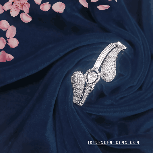 An exquisite silver bracelet featuring a teardrop-shaped diamond at the center, surrounded by intricate stone detailing, elegantly displayed on deep navy velvet with soft pink floral petals.